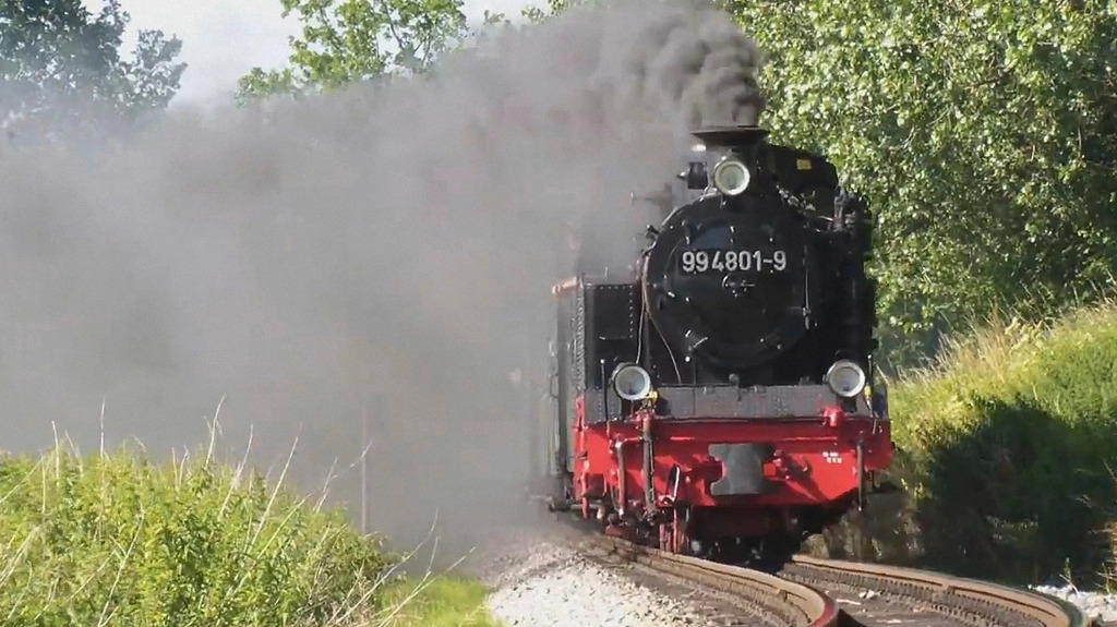 Vintage steam locomotive releasing a cloud of steam beside an iron platform
