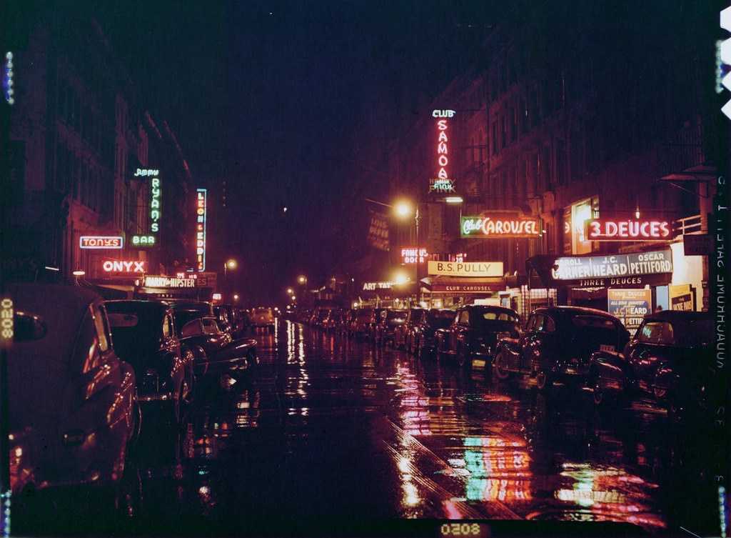 Rain-slicked city street at night reflecting magenta and cyan neon signs